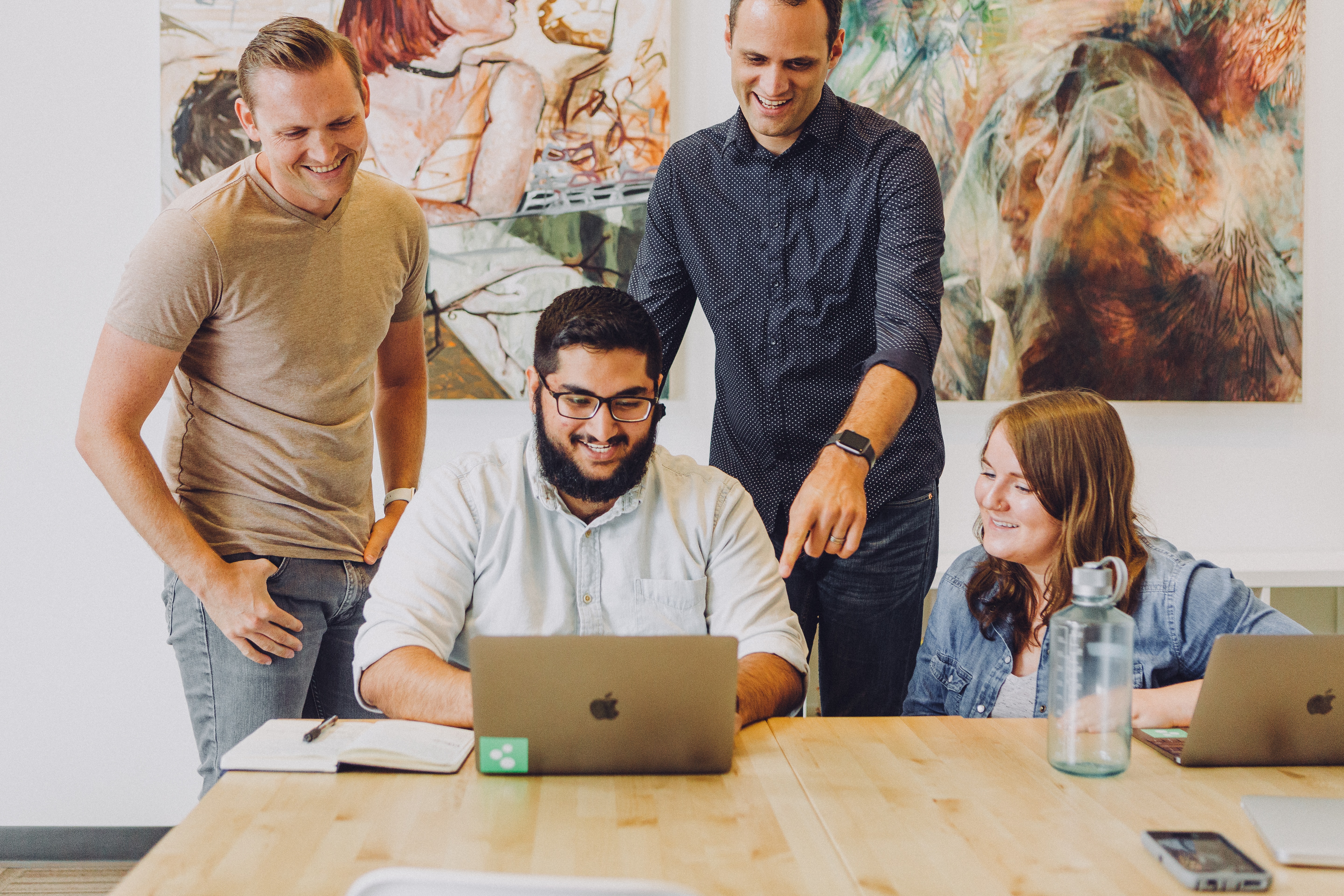 4 people looking at laptop smiling in office