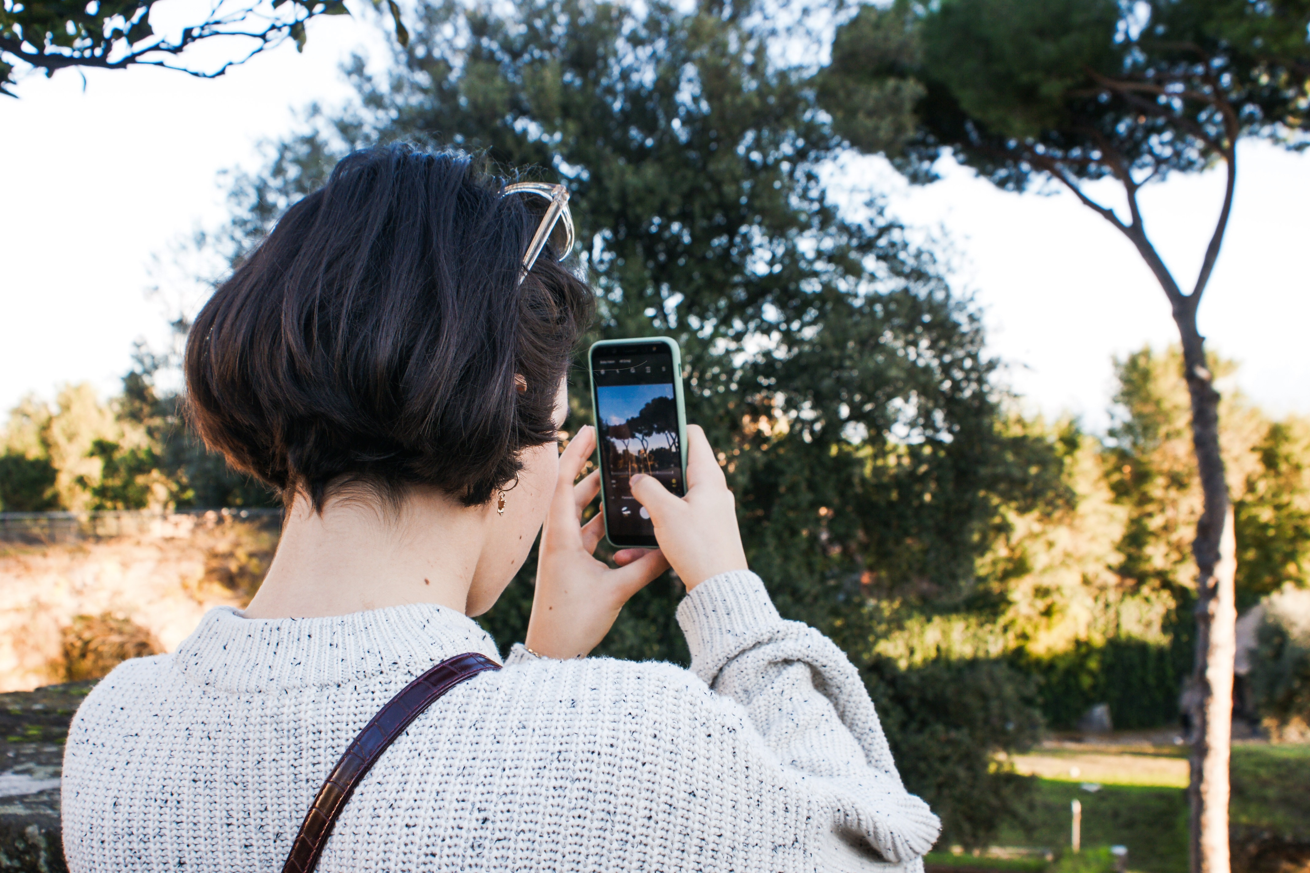 Short haired girl taking picture on phone of nature