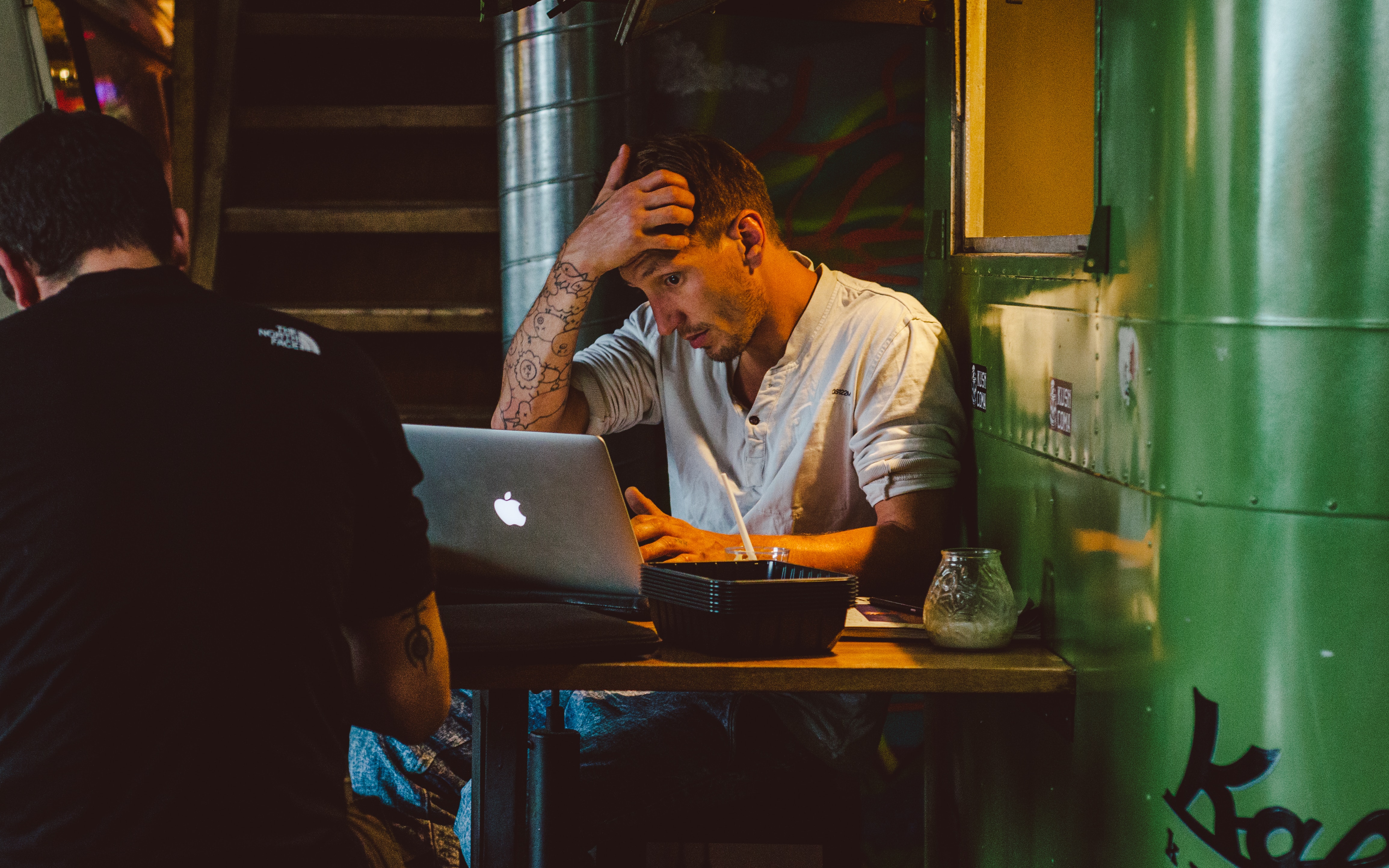 Tattoo guy sitting in a bar with Mac laptop scratching head